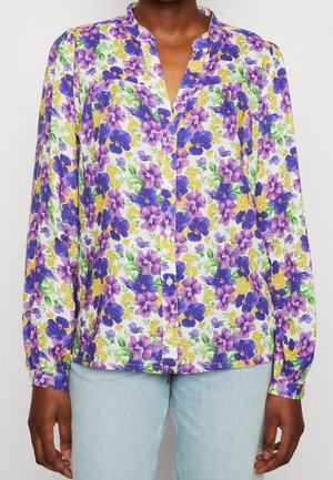 Blusa floreale con scollo a V, caratterizzata da visceri viola e accenti gialli su uno sfondo bianco. Maniche lunghe con polsini a bottone.