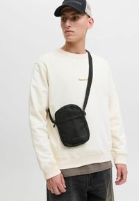 Sort crossbody taske lavet af stof med en glat tekstur. Har en lynlåslukning, justerbar rem og logo detaljer på forsiden.