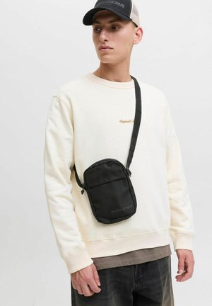 Sac bandoulière noir en tissu avec une texture lisse. Doté d'une fermeture zippée, d'une sangle réglable et de détails de logo à l'avant.