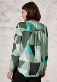 Blusa a maniche lunghe con un motivo geometrico in verde menta, nero e teal. Realizzata in tessuto leggero con dettaglio arricciato sul retro.