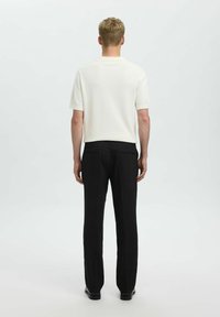 Maglietta bianca a maniche corte in maglia e pantaloni neri, slim fit, texture liscia, con dettagli di cucitura sottili. Nessun motivo o accento prominente.