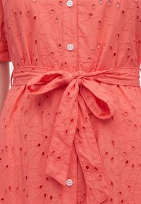 Coral dress with eyelet floral embroidery, front buttons, and a tied fabric belt at the waist.