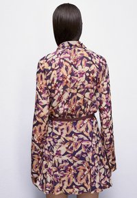 Abito a stampa floreale in viola, beige e arancione. Presenta maniche lunghe, un colletto e una cintura marrone in vita con gonna svasata.