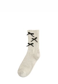 Knit cream sock with ribbed texture, featuring three black decorative bows along the outer side for accent.