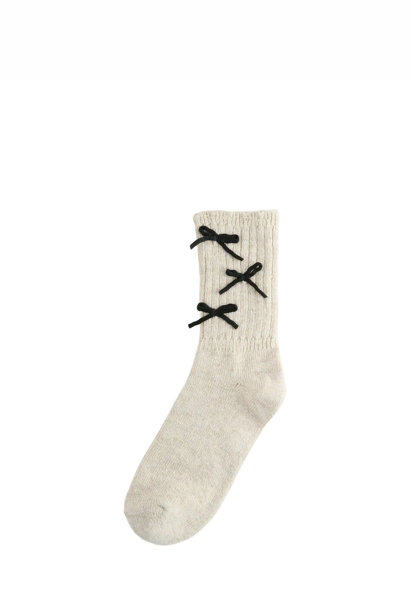 Knit cream sock with ribbed texture, featuring three black decorative bows along the outer side for accent.