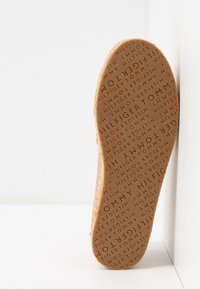 Semelle d'une chaussure Tommy Hilfiger beige avec un motif de texte « TOMMY HILFIGER » répété dans différentes orientations.