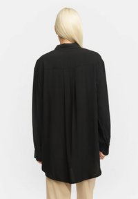 Musthave musta pika varrukaga särk, millel on lõdvestatud lõige. Omab kraed, nööpe küünarnukkidel ja taga voldikut. Valmistatud siledast ja voolavast kangast.