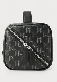 Svart veske med geometrisk mønster, featuring en skrå glidelås, sølvfarge detaljer og en strukturert overflate. Håndtak på toppen for enkel bæring.