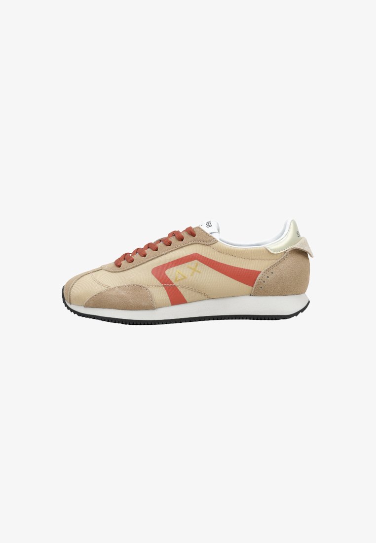 Zapatilla beige y tostada con cordones color óxido, una franja roja angular, logotipo geométrico amarillo, forro interior blanco y suela negra.