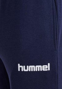 Marineblå bomuldsjoggers med en glat tekstur, sidelommer og hvid "hummel"-logo trykt på låret.