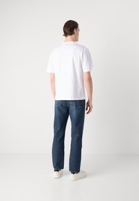 T-shirt en coton blanc avec une coupe droite, associé à un jean en denim bleu foncé. Le look est complété par des baskets blanches.
