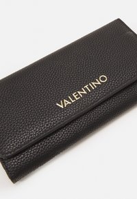 Juodos odos piniginė su tekstūruota paviršiumi. Pirmame pusėje yra auksinis "VALENTINO" logotipas ir sulankstomas užtrauktukas.