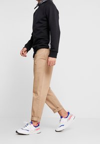 Sudadera negra con panel lateral gris, pantalones caqui y zapatillas blancas con acentos coloridos. Tejido suave, corte relajado, diseño informal.