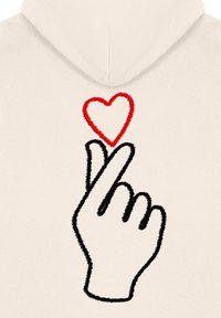 Sudadera beige con un diseño bordado que presenta un contorno negro de una mano haciendo un corazón con los dedos sobre una forma de corazón roja.