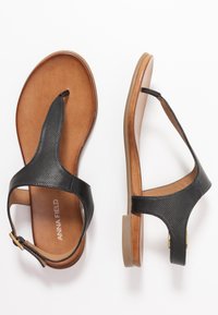 Sandalias de tiras negras con una correa texturizada y una plantilla de cuero marrón. Cuentan con un pequeño tacón y herrajes con detalles en dorado en la correa del tobillo.