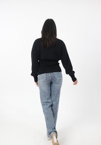 Schwarzer Pullover mit langen Ärmeln, gerippten Bündchen und einem taillierten Bund, kombiniert mit hochgeschnittenen blauen Jeans.