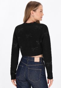 Maglione nero corto realizzato in materiale peloso con motivi a stella e colletto a costine, abbinato a jeans in denim scuri a vita alta.