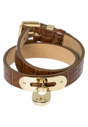 Brązowy skórzany pasek zapinany na złotą sprzączkę z zawieszką w kształcie kłódki z wygrawerowanym napisem "Michael Kors."