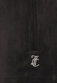 Top in velluto nero con design a mezza zip, caratterizzato da un logo di strass sulla parte anteriore. Texture liscia con una leggera lucentezza.