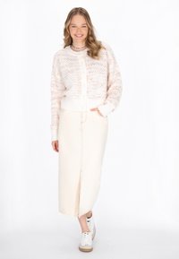 Pleteni pastelnorozni cardigan z gumbi, v kombinaciji s kremnim maksi krilom z razporkom in belimi supergami.