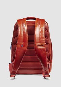 Mochila de cuero rojo con respaldo acolchado, correas anchas y herrajes metálicos. Presenta detalles texturizados y tiradores de cremallera azules.