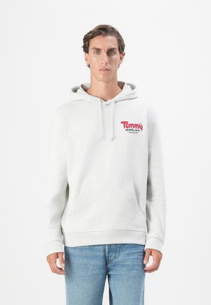 Grauer Kapuzenpullover aus weichem Material, mit einer frontalen Tasche und rotem "Tommy Jeans"-Logo. Enganliegende Bündchen an den Ärmeln und am Saum.