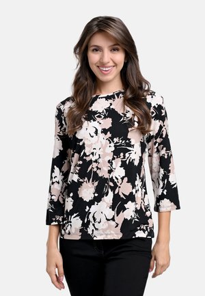 Schwarz blumige Bluse mit 3/4-Ärmeln, die große rosa und weiße Blumenmuster zeigt. Hergestellt aus weichem Stoff mit einem runden Ausschnitt.