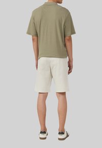 Polo shirt verde a righe con maniche corte, abbinato a pantaloni corti bianchi e sneakers in bianco e nero. Focus sulla texture e sul design casual.
