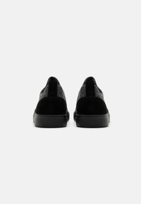 Fekete velúr és szürke filc sneakers, texturált felülettel, lapos gumi talppal, és hátsó húzófülekkel a könnyű felvétel érdekében.