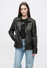 Zwarte leren jas met een klassieke kraag, ritssluiting en zijzakken. Strak ontwerp met een subtiele glans, gecombineerd met lichtblauwe spijkerbroek.