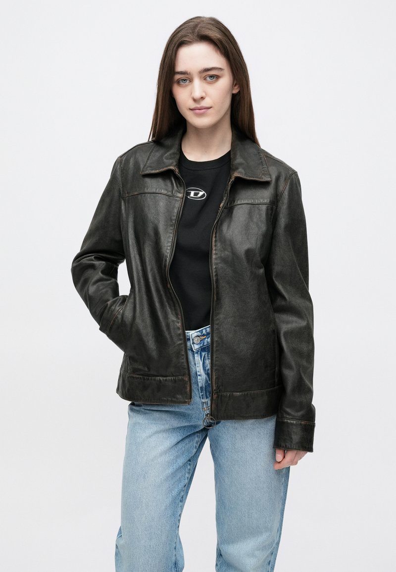 Black leather jacket with a classic collar, zip closure, and side pockets. Fitted design with subtle sheen, paired with light blue jeans.