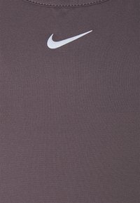 Top sportivo viola in materiale rigato, con logo Nike bianco. Il design è aderente e presenta una texture liscia.