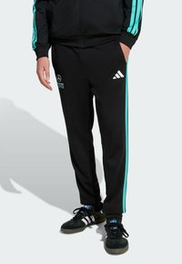 Pantalon de jogging noir avec des bandes latérales turquoise, en tissu doux, avec un logo imprimé sur la cuisse et des poches élastiques aux chevilles.