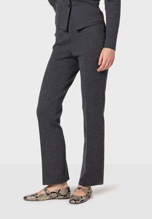 Donkergrijze tapered broeken van een zachte stof, gecombineerd met zwart-gouden flats met een slangenpatroon en een bandje bovenop.