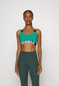Sostén deportivo verde con escote cuadrado y tirantes negros que presentan la marca en blanco "NEBBIA". Llevado con leggings oscuros de talle alto en verde.