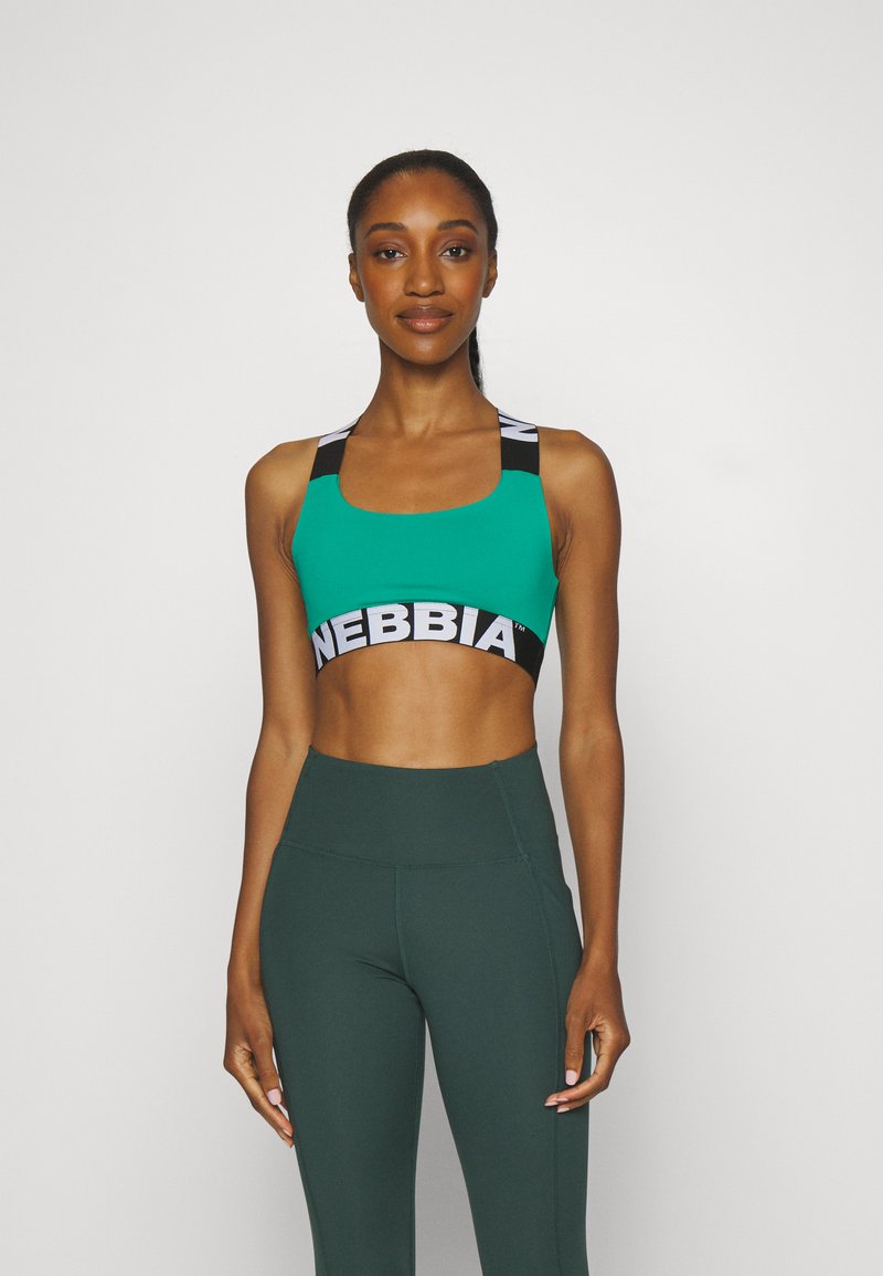 Sostén deportivo verde con escote cuadrado y tirantes negros que presentan la marca en blanco "NEBBIA". Llevado con leggings oscuros de talle alto en verde.