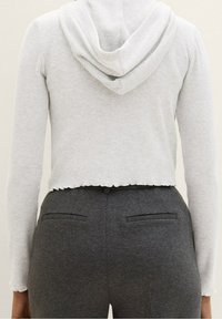 Krótkia, jasnoszara bluza z kapturem o prążkowanej teksturze. Posiada kaptur i falowany dół, zestawiona z dopasowanymi ciemnoszarymi spodniami z tylnymi kieszeniami.