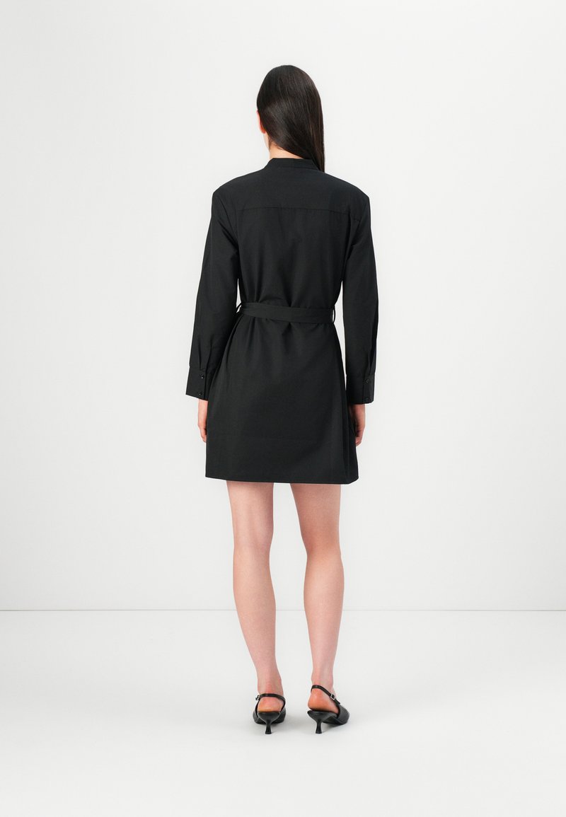 Schwarzes Hemdkleid mit langen Ärmeln, geknöpften Manschetten und einem gebundenen Taillengürtel. Glatter Stoff mit einer figurbetonten Silhouette und Kragen im Hemd-Stil.
