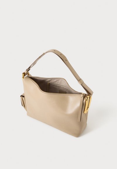Sac à main en cuir beige avec large bandoulière réglable et fermeture éclair dorée visible, présenté ouvert pour révéler une poche intérieure zippée.