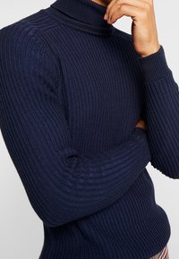 Navy ribbed turtleneck sweater made of thick knit fabric. Features long sleeves and a fitted design, emphasizing texture and warmth.