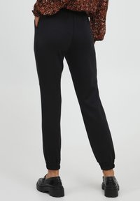 Zwarte joggingsbroek met elastische tailleband, taps toelopende benen, omgeslagen enkels en zijzakken. Draagt met zwarte plateau schoenen.