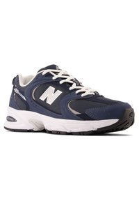Scarpa sportiva blu navy realizzata in mesh e materiale sintetico. Presenta lacci bianchi, dettagli grigi e una suola in gomma nera con motivi di trazione.