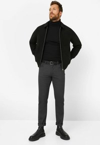 Zwarte ritsjack over een zwarte coltrui, grijze tapered broek en zwarte enkellaarsjes met een stevige zool. Eenvoudig design, geen zichtbare patronen.