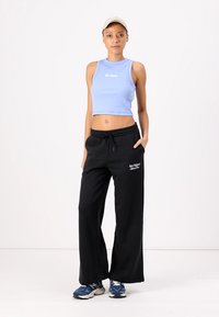 Gaiši zils bez piedurknēm cropped tops ar baltu logo; melnas platas bikses ar sānu kabatām; zilas sporta apavi. Mīksti, ikdienišķi audumi.