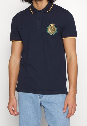 Polo bleu marine en coton, avec un col agrémenté d'accents jaunes et rouges, des manches courtes, et un logo brodé sur la poitrine.