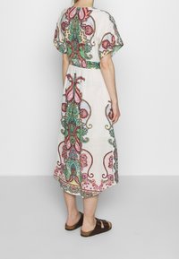 Długa, luźna sukienka z lekkiego materiału, ozdobiona żywymi wzorami paisley w odcieniach różu, zieleni i niebieskiego. Całość dopełniają brązowe sandały.