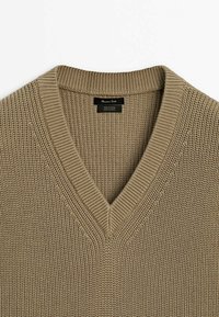 Beige knitted V-neck sweater with ribbed collar, made of cotton, shown from top down, highlighting texture and stitching details.