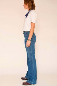 Jean évasé bleu clair à taille haute, associé à un t-shirt blanc à manches courtes et un bandana bleu à motifs. Chaussures marron.