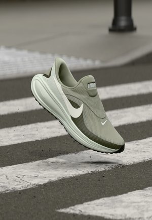 Lys grønn Nike-sneaker med teksturert mesh overdel, hvit swoosh og en støtabsorberende såle, svever over et fotgjengerfelt.