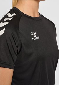 Mustapaita, jossa on lyhyet hihat, pyöreä kaula-aukko ja valkoiset olkaimet. Hummelin logo näkyy valkoisena rinnassa.